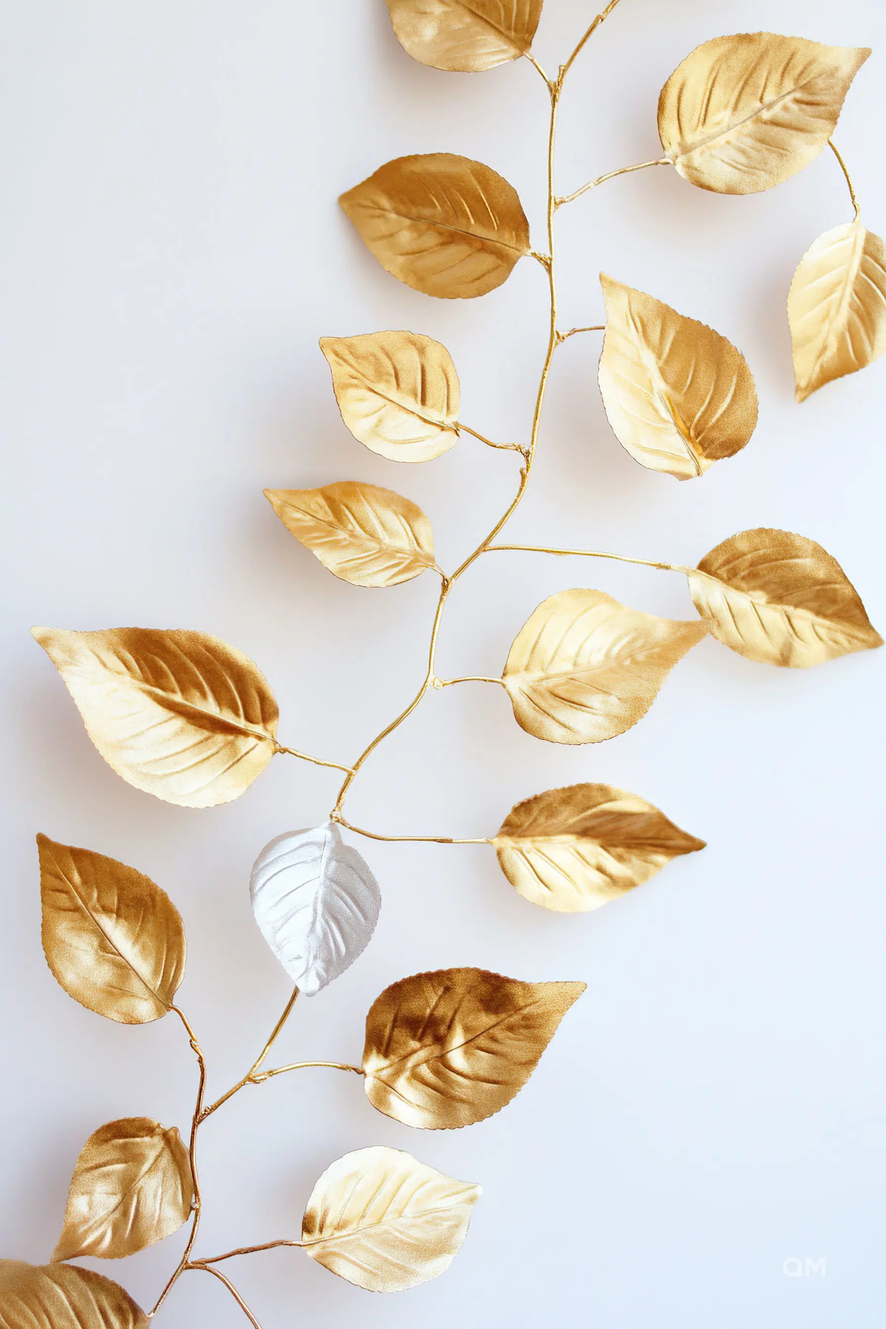 A branch with golden leaves against a white background, with one leaf in a contrasting silver color.