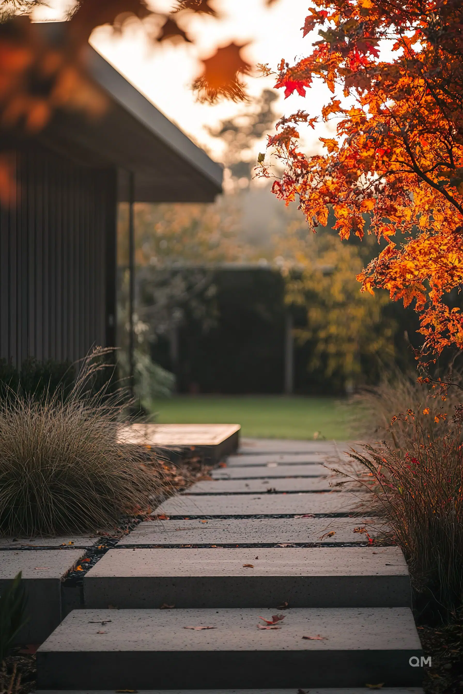 Concrete stepping stones lead to a modern house surrounded by autumn foliage at dusk.