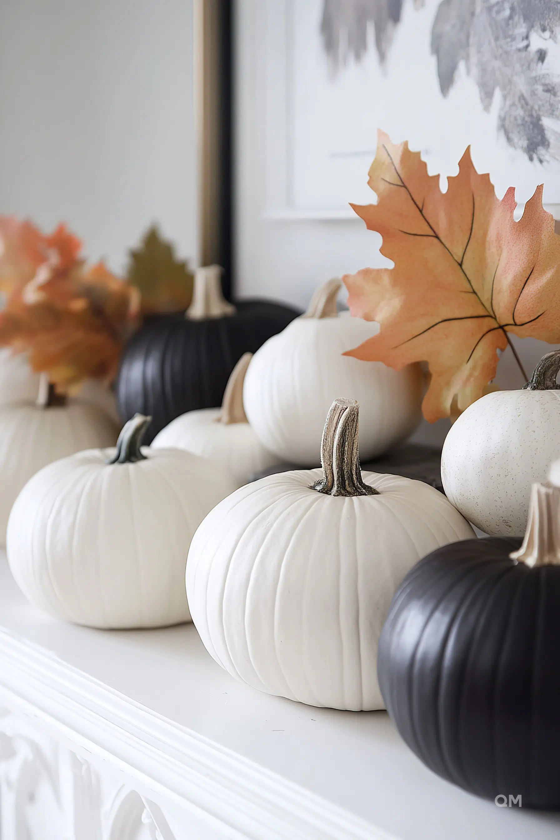 Decorative white and black pumpkins arranged on a mantel with autumn leaves, showcasing a fall aesthetic.