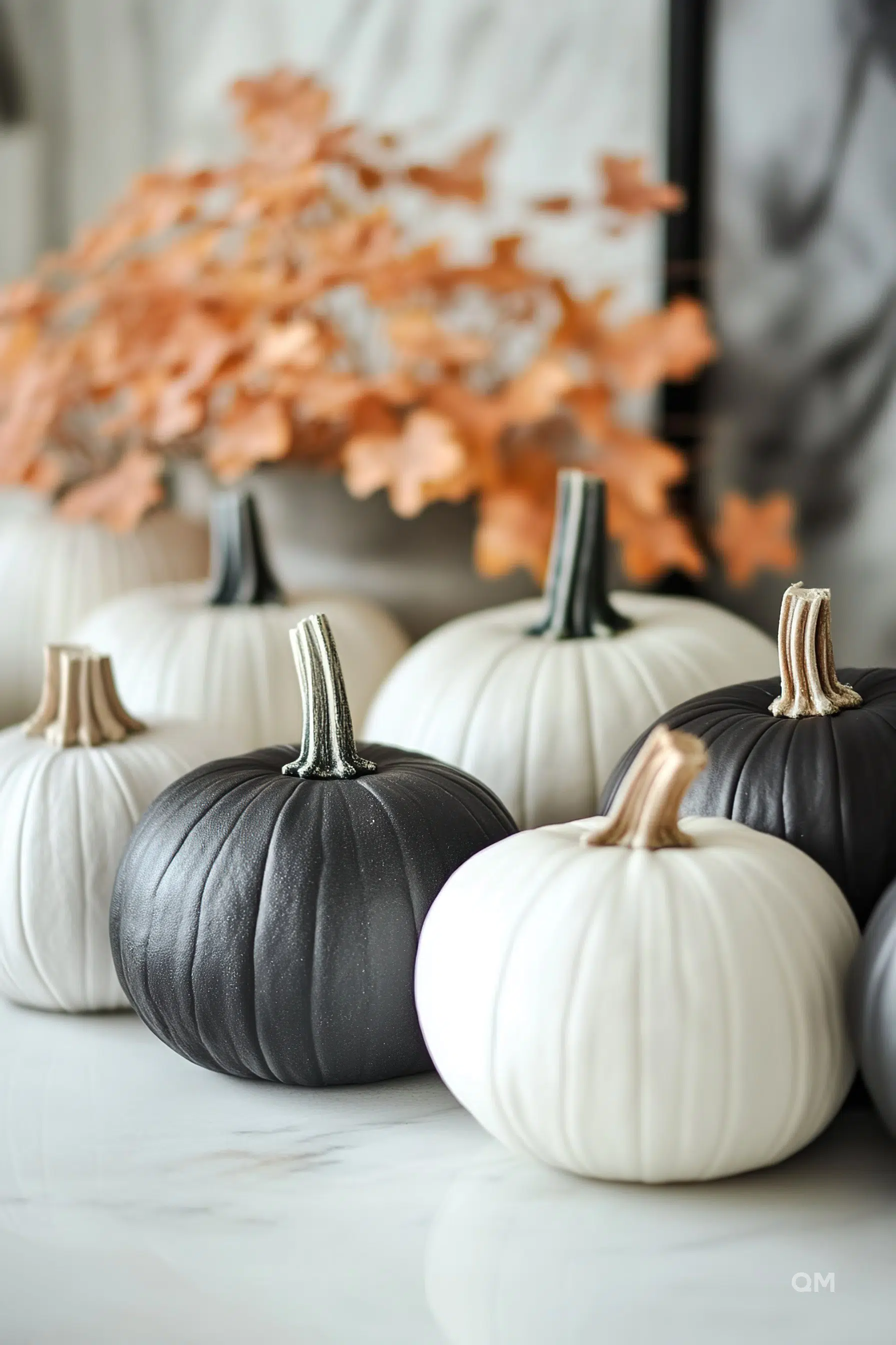 A collection of black and white decorative pumpkins on a marble surface with blurred autumn leaves in the background.