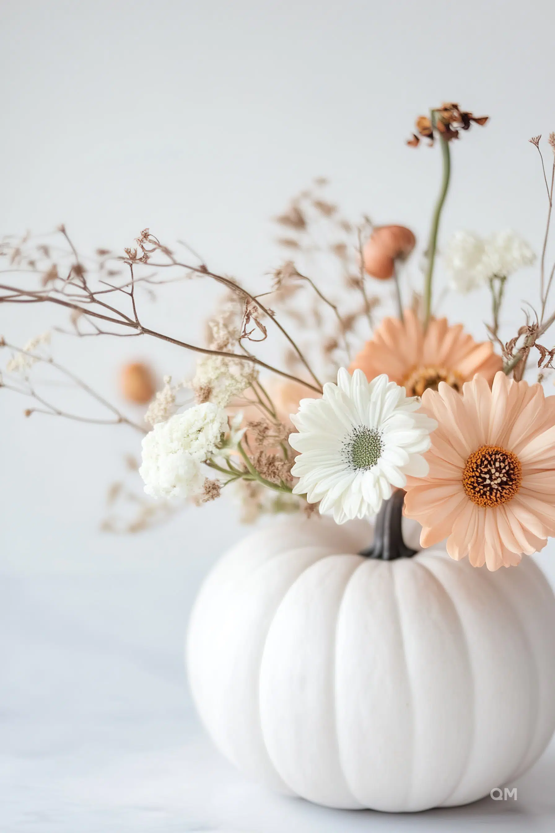 ALT: A white pumpkin vase with a bouquet of pastel flowers, including white and peach gerberas, on a light background.
