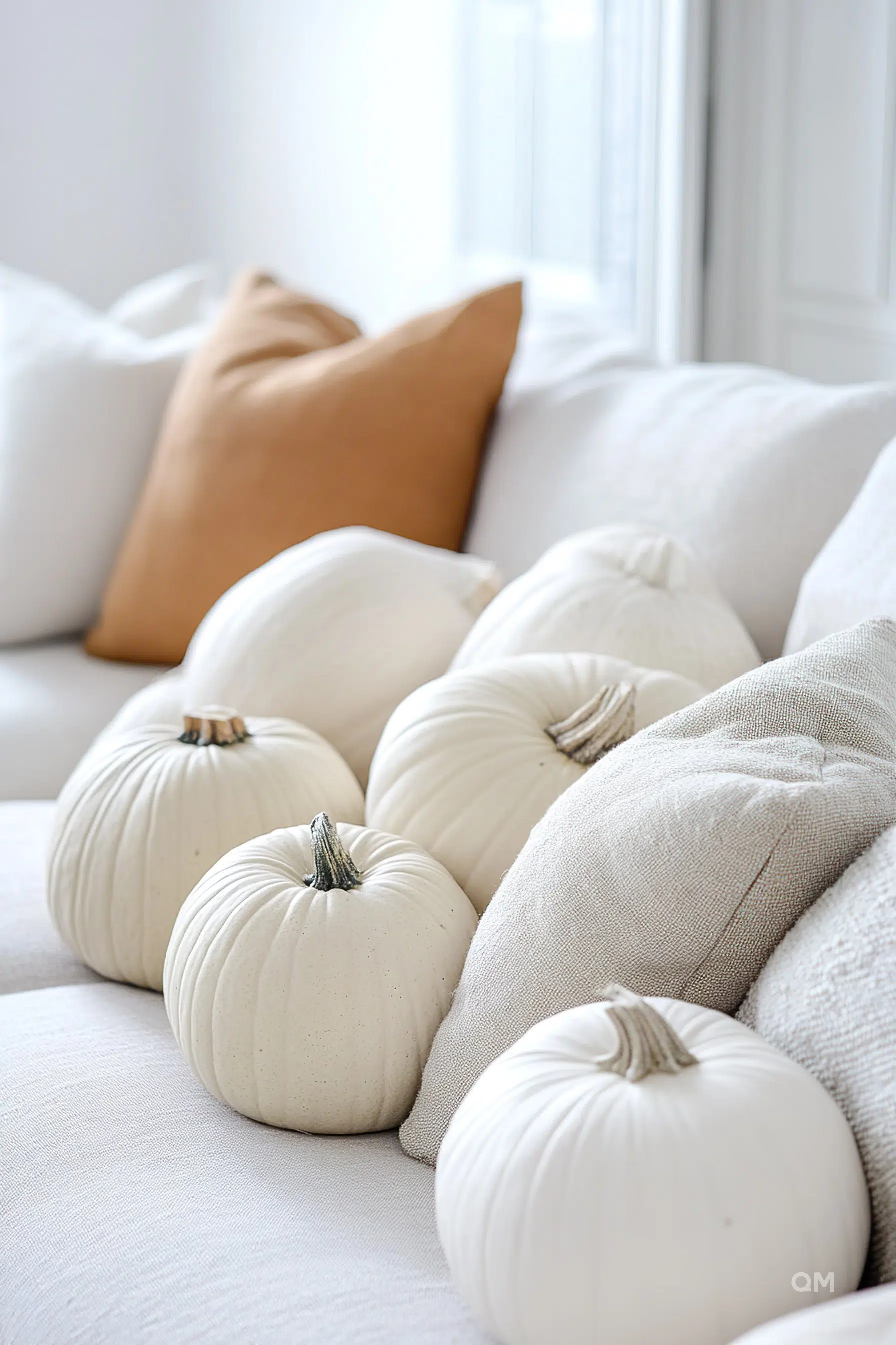 ALT: White pumpkins artfully arranged on a cozy sofa with white and beige pillows, in a bright, airy room.