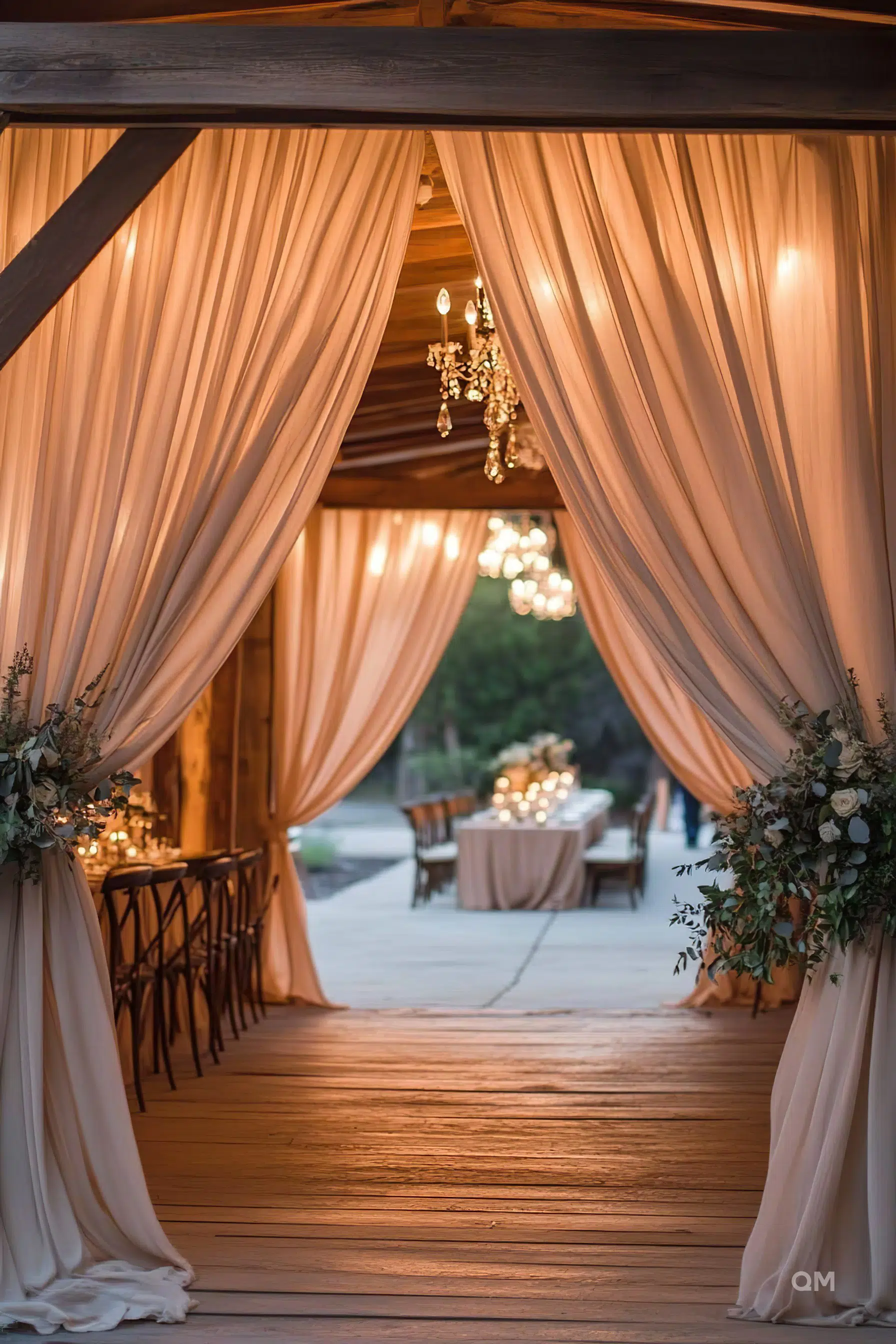 Elegant outdoor wedding venue entrance draped with sheer curtains, chandeliers, and dimly lit tables set in the background.