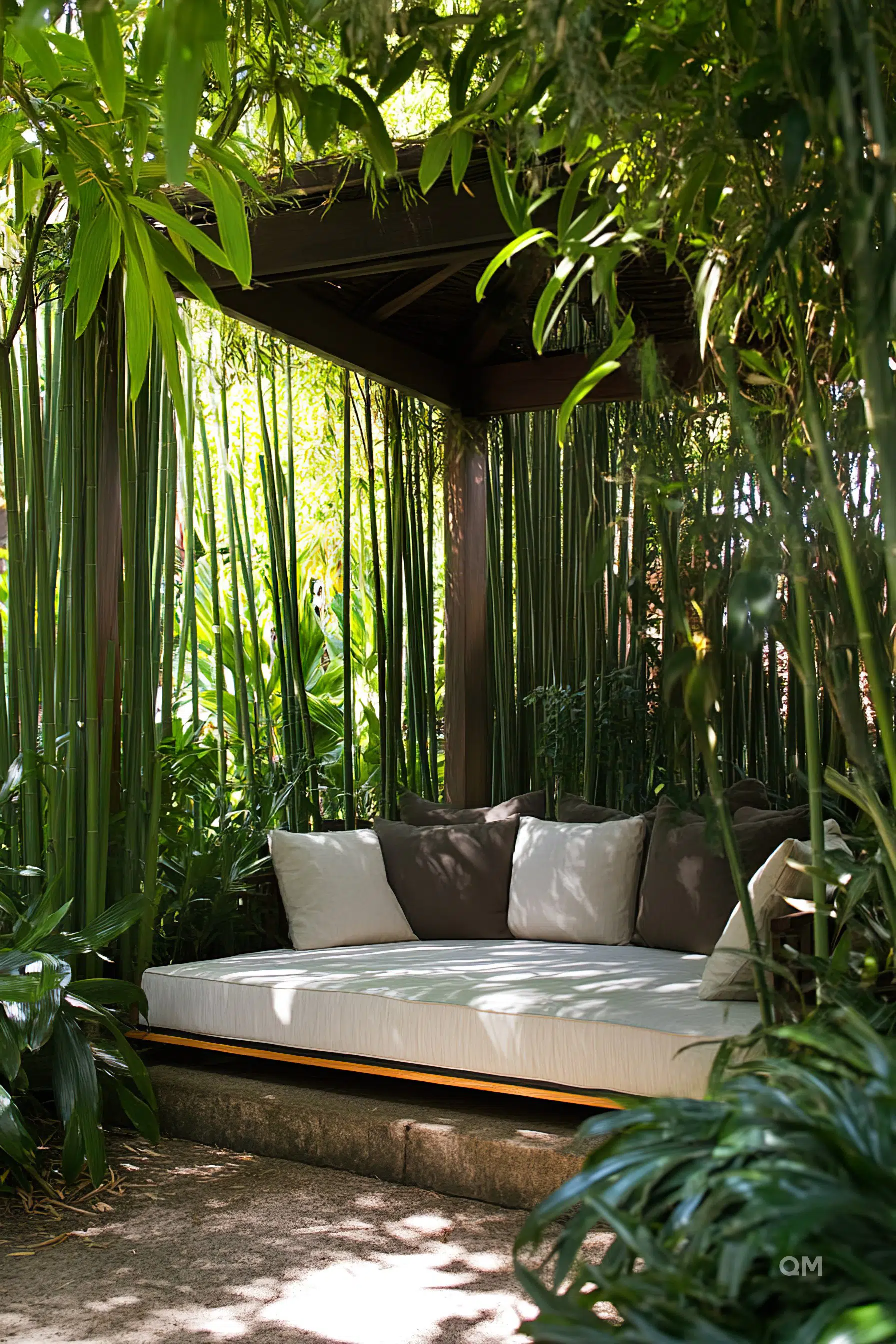 A cozy outdoor lounge bed with cushions under a wooden canopy, surrounded by lush green plants and bamboo.