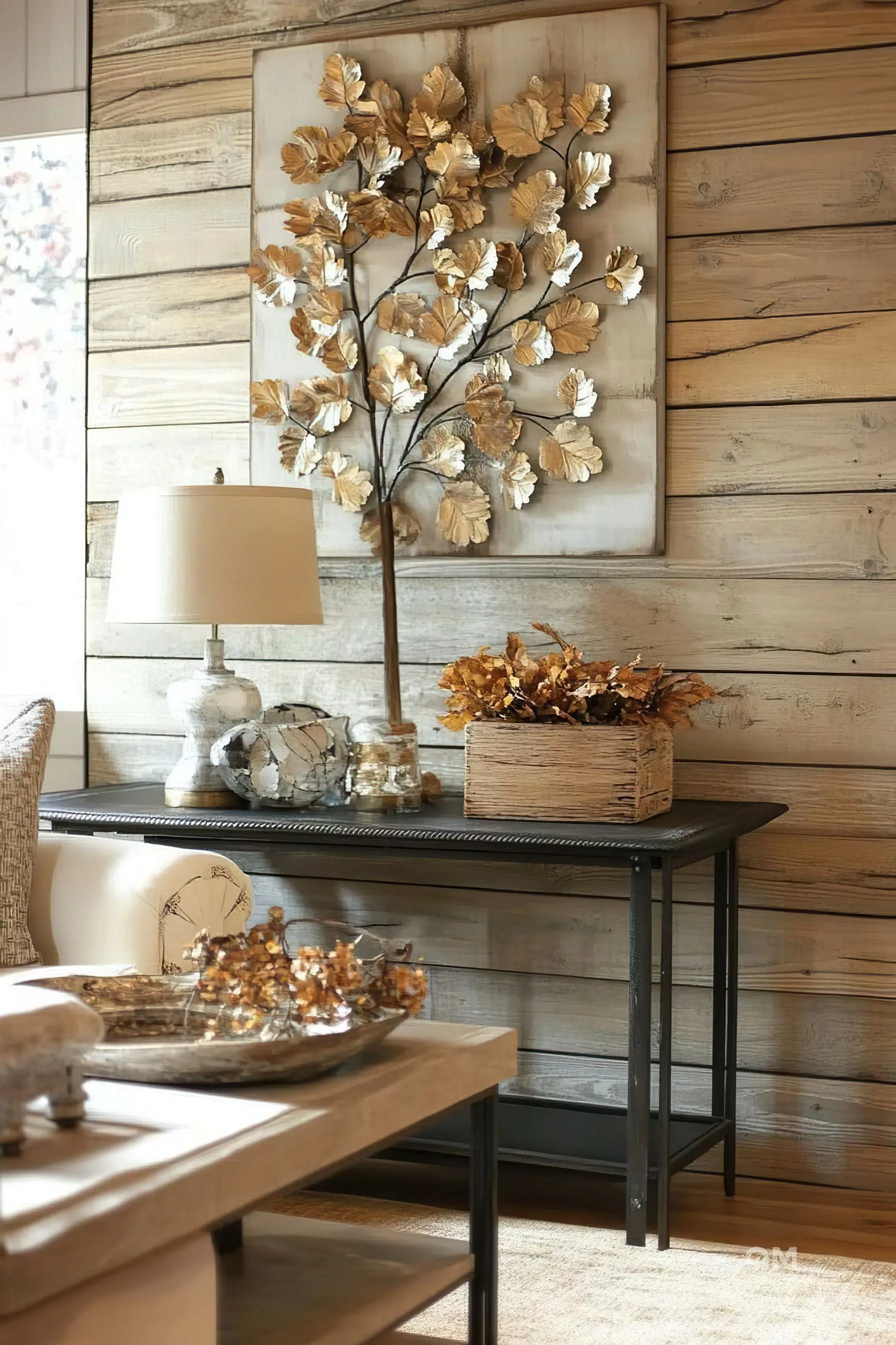Rustic-style interior with a metallic tree wall art on a distressed wooden panel, table lamp, decorative vases, and dried flowers on a console table.