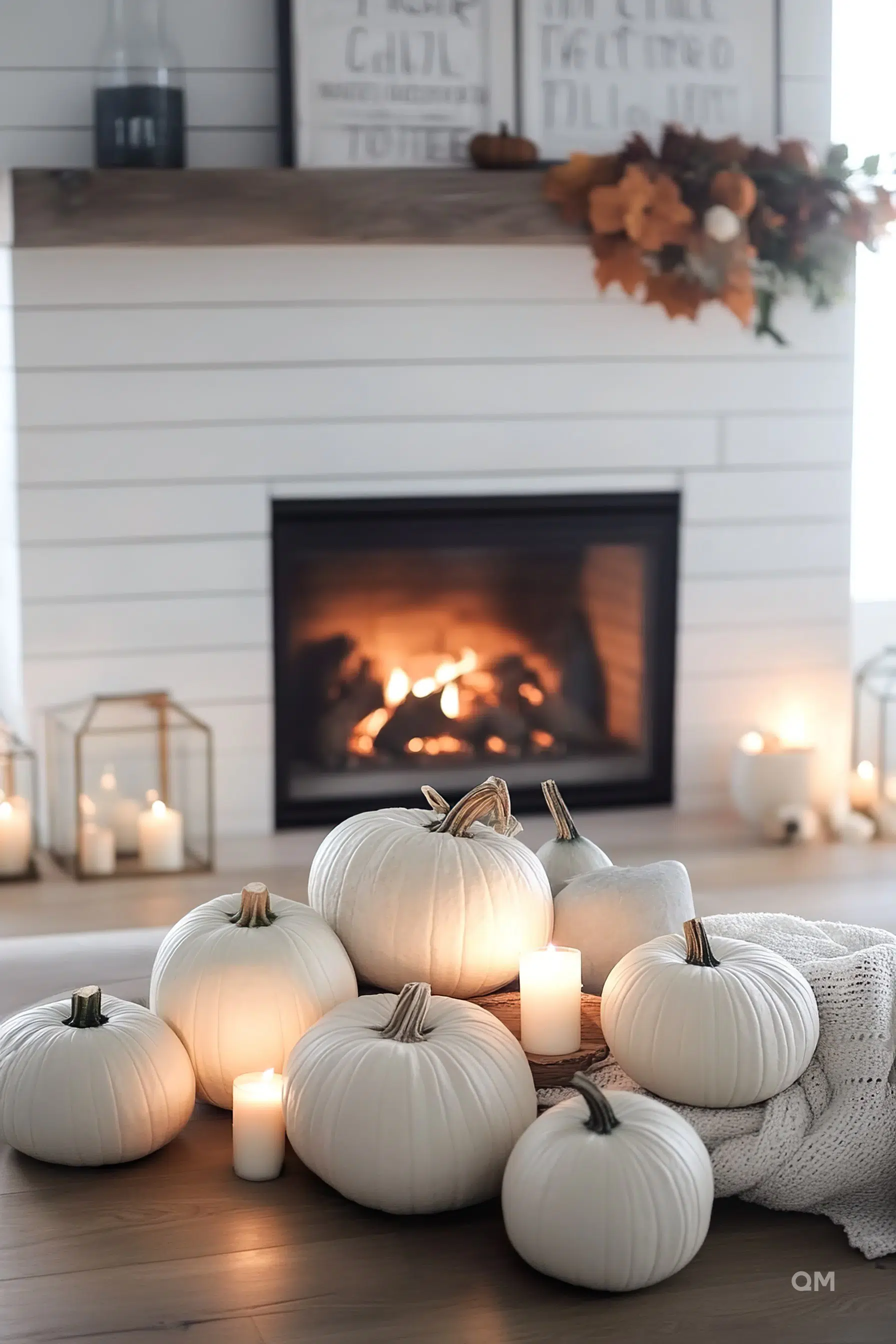 Cozy autumn setting with white pumpkins on the floor surrounded by lit candles, with a fireplace in the background.