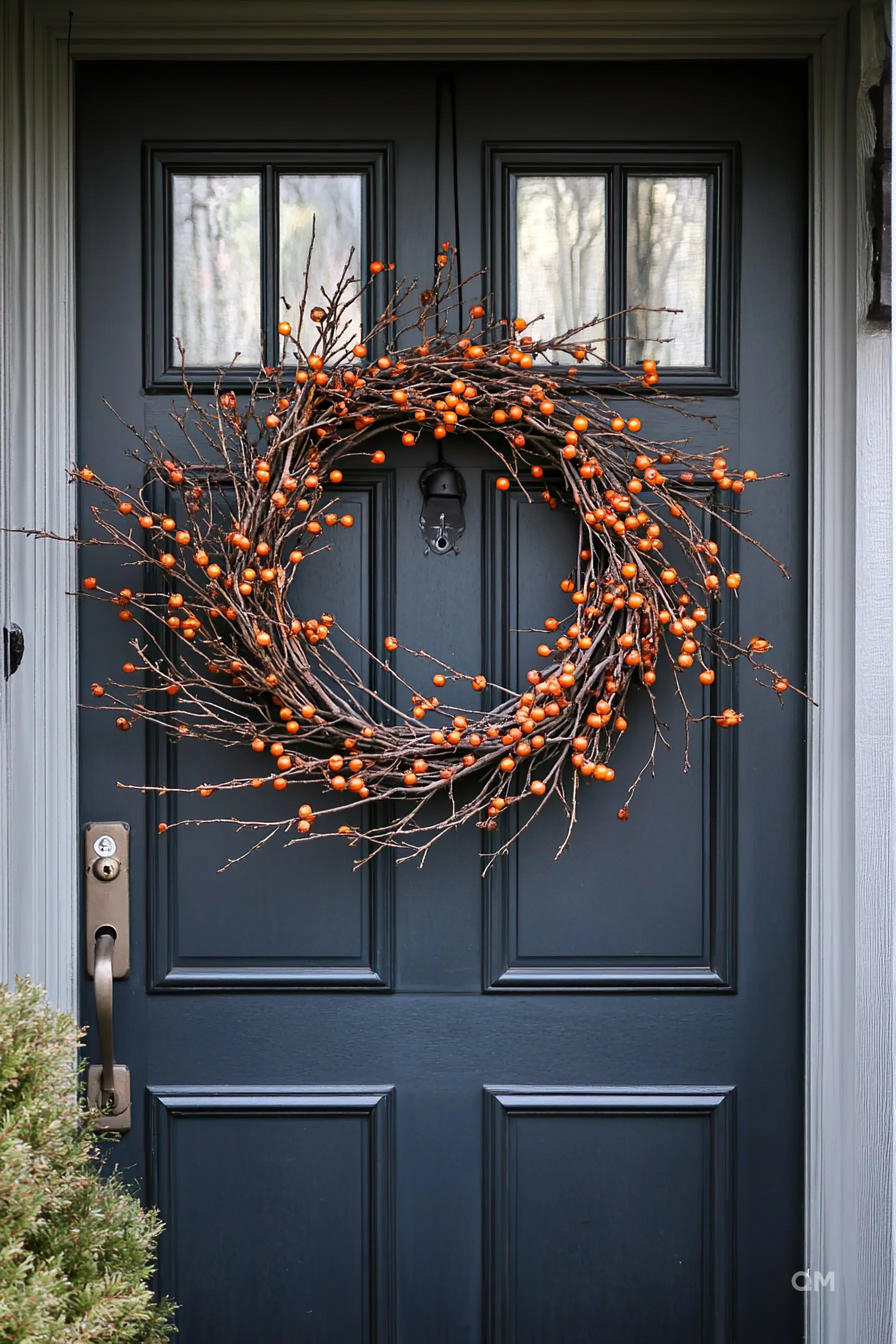 A dark blue front door adorned with a large, twig wreath featuring small orange berries, giving a warm, seasonal touch.