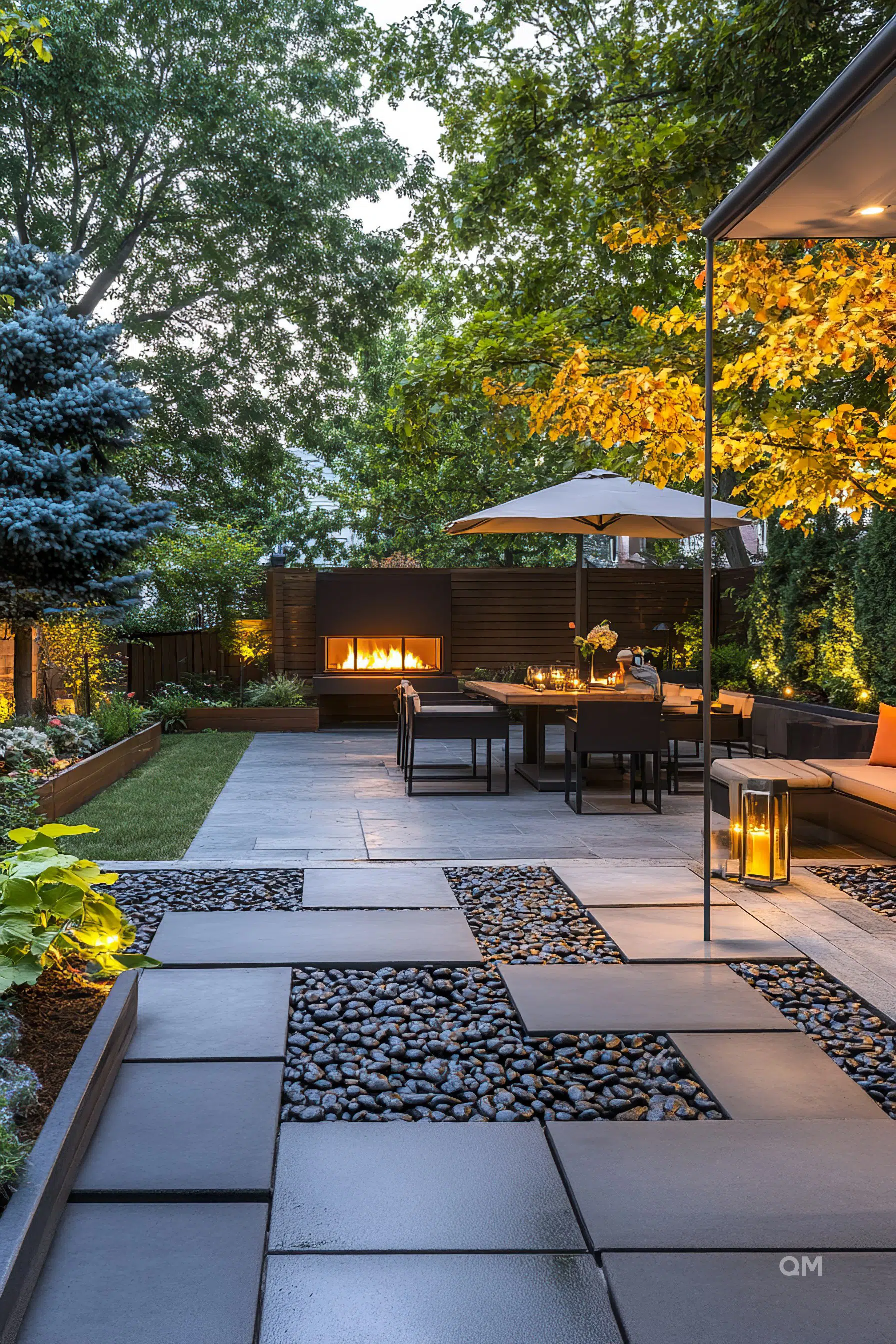 Elegant outdoor living space with modern furniture, fire pit, patio umbrellas, and ambient lighting surrounded by lush greenery and trees.