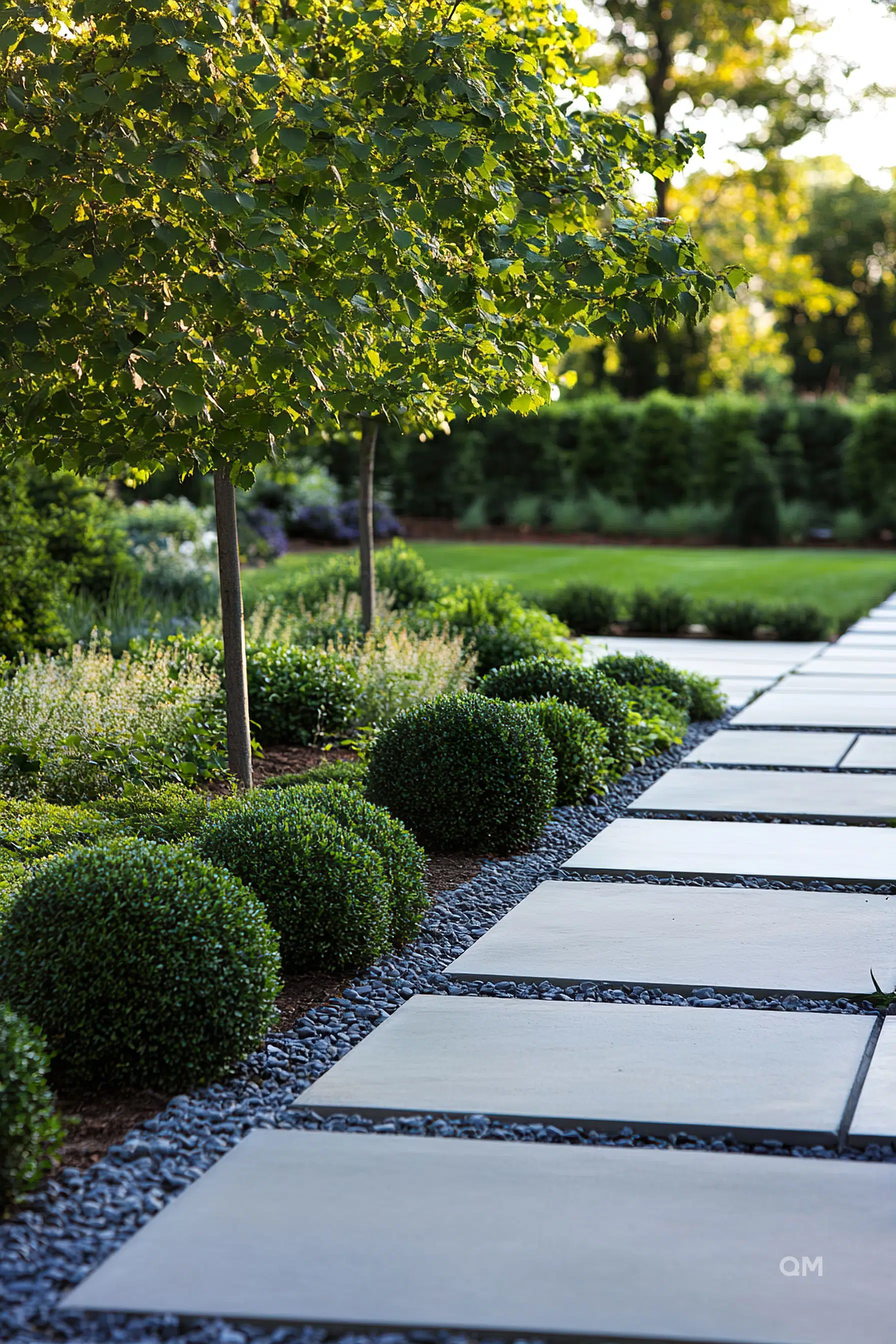 A neatly landscaped garden pathway with square stepping stones, surrounded by trimmed round bushes and young trees.