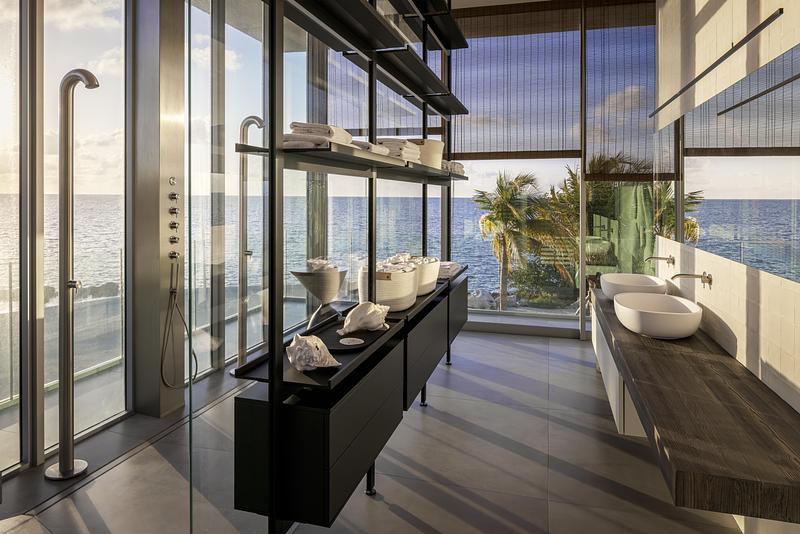 primary bathroom open steel shelving with conch shells and ceramic objects styled against full-height ocean-view glazing