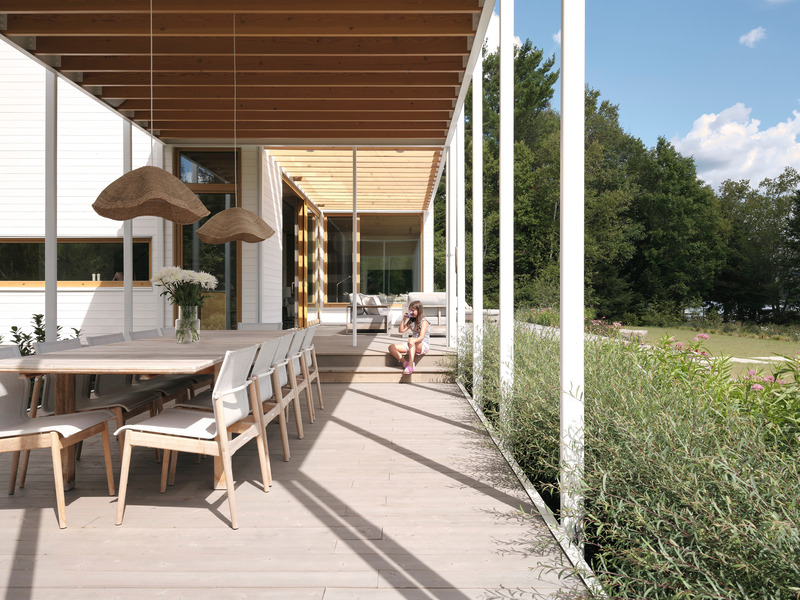 outdoor veranda dining area with long wood table, sling chairs, rattan pendant lights, exposed cedar pergola ceiling, an