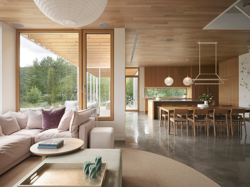 open-plan living and dining interior with polished concrete floor, pale wood ceiling, floor-to-ceiling oak-framed window