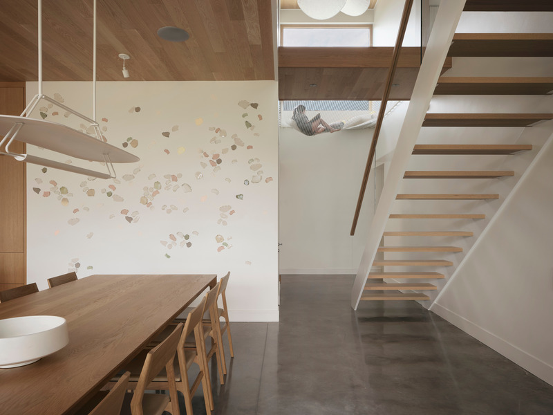 dining area with open-tread oak stair, white steel stringer, white pebble-motif art wall, polished concrete floor, and c