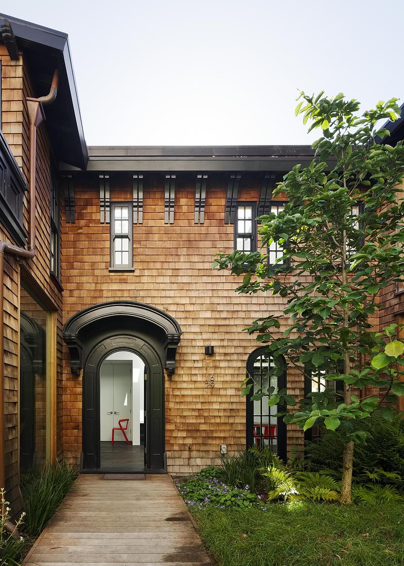 garden courtyard entry with black ornate arched front door open to white interior, cedar shingle facade, timber deck pat