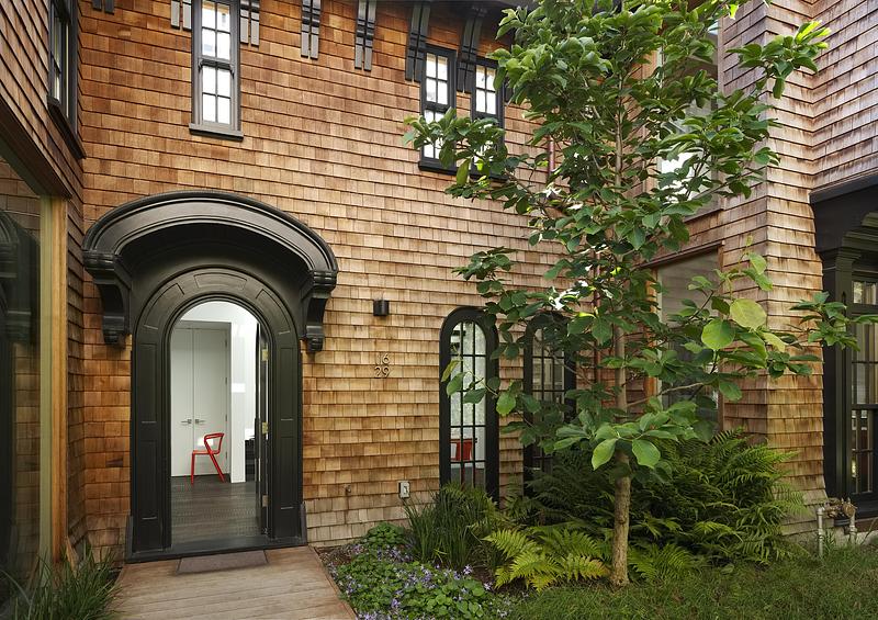 daytime courtyard exterior showing black ornate arched entry door numbered 1629, adjacent arched grid window with red ch