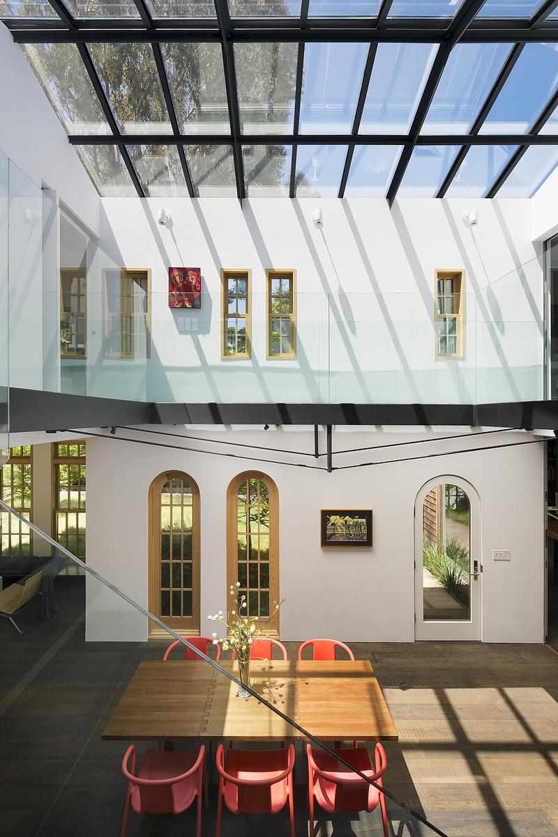 overhead view into glass roof dining volume showing black steel grid glazing casting shadow lattice, glass balustrade up