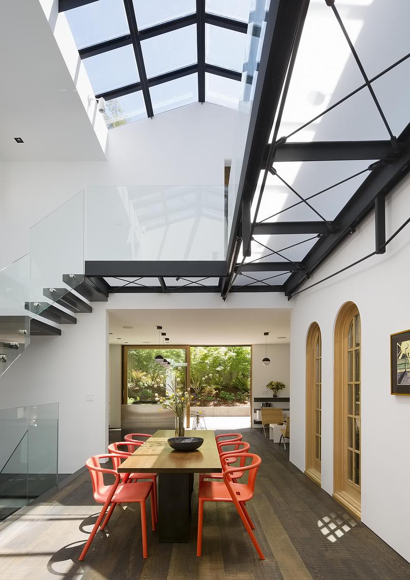 upper-landing view of glass roof interior with black steel mullion shadow grid on white curved wall, glass balustrade, s
