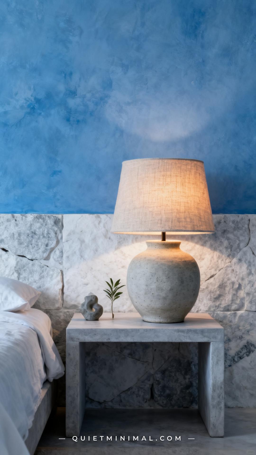 A wide bedroom composition showing a simple nightstand with a stone-finish ceramic table lamp as the dominant visual ele