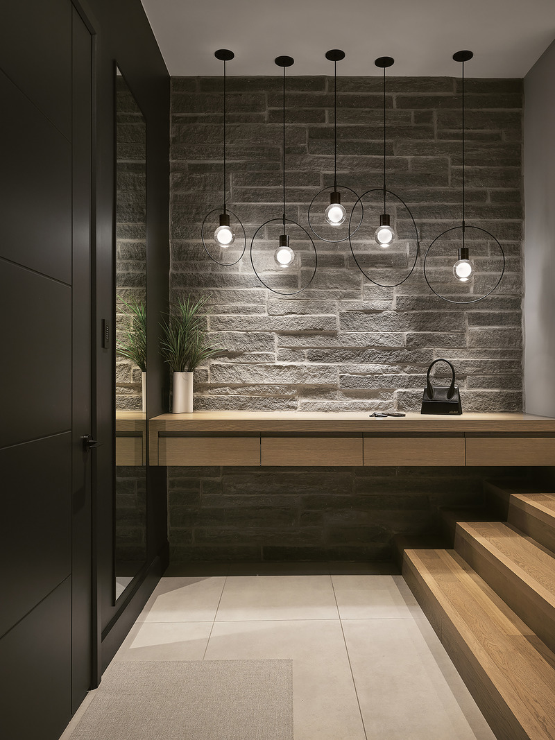 entryway foyer with raw grey stone accent wall, floating oak console with drawer, five circular black ring pendant light