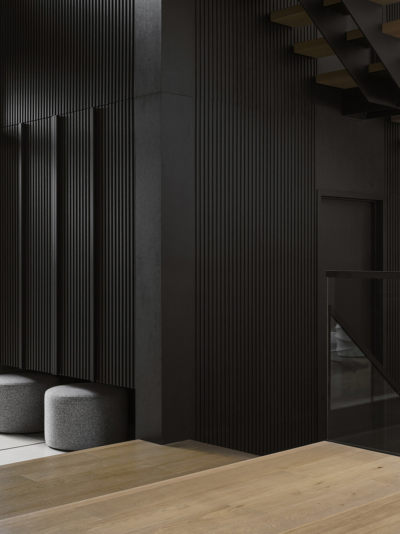 entry hall detail showing floor-to-ceiling black fluted wood panels, two round grey boucle ottomans, pale oak plank floo
