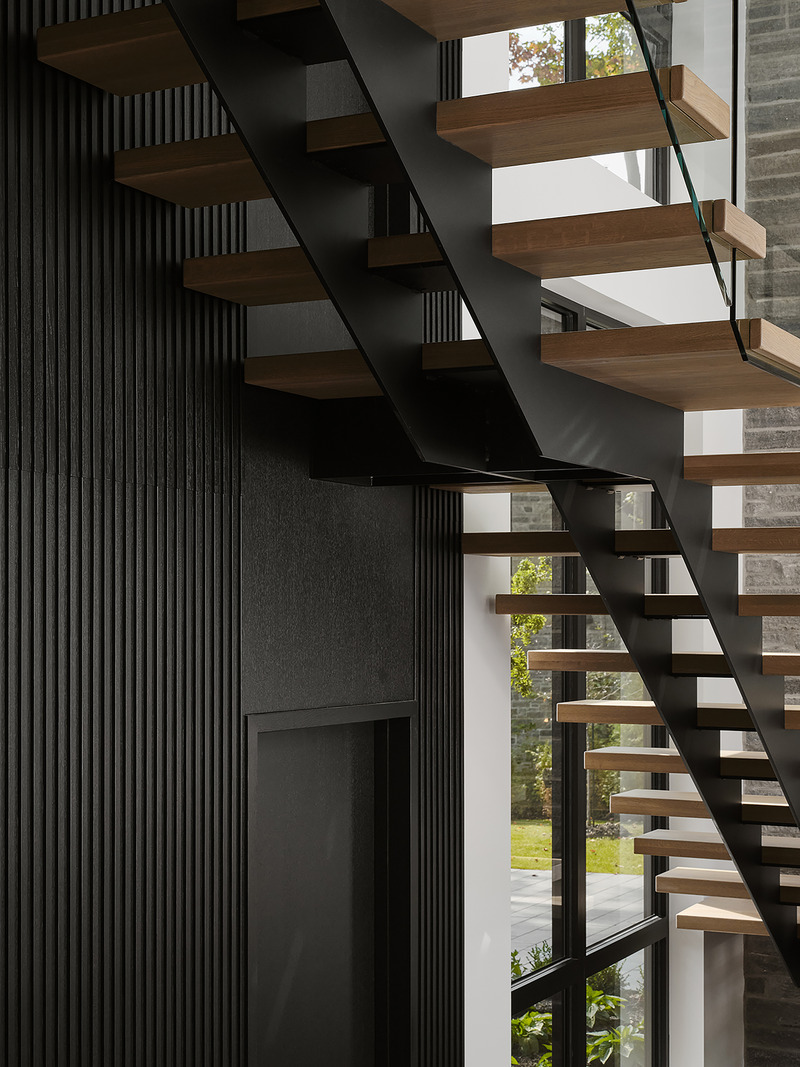 open-riser staircase with warm oak treads cantilevered from black steel stringer, glass balustrade panel, dark fluted wo
