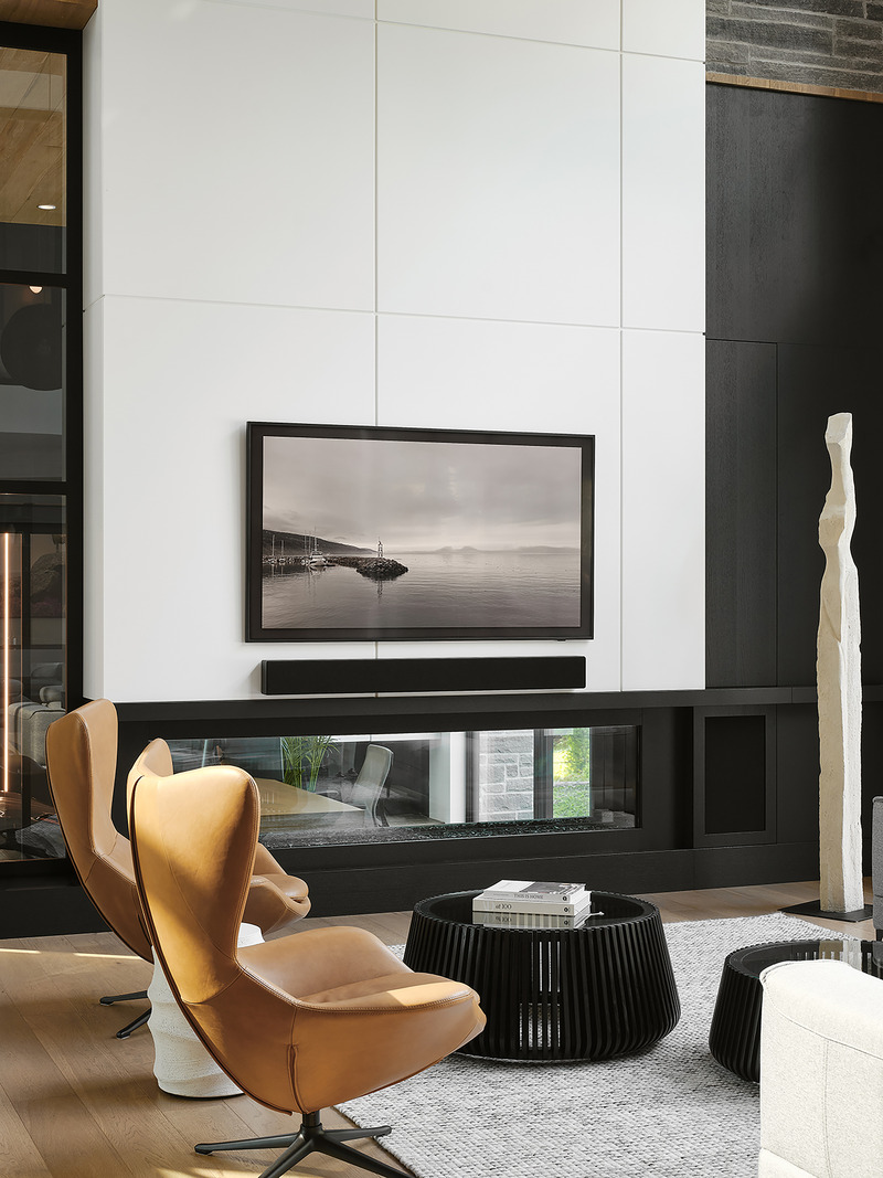 living room media wall with large white panel tiles, framed landscape artwork above linear fireplace, amber leather loun