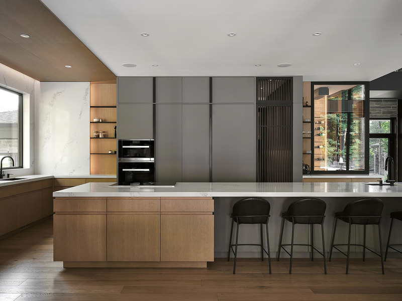kitchen with long white stone waterfall island, natural oak lower cabinetry, matte grey upper cabinets flanking black do