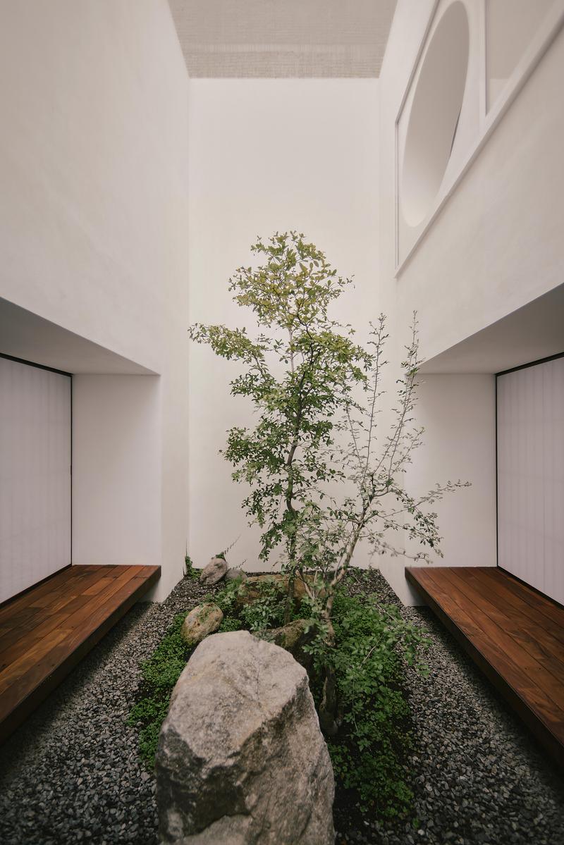 interior courtyard stone garden with single slender tree, large rough boulders on grey gravel, flanking dark wood platfo