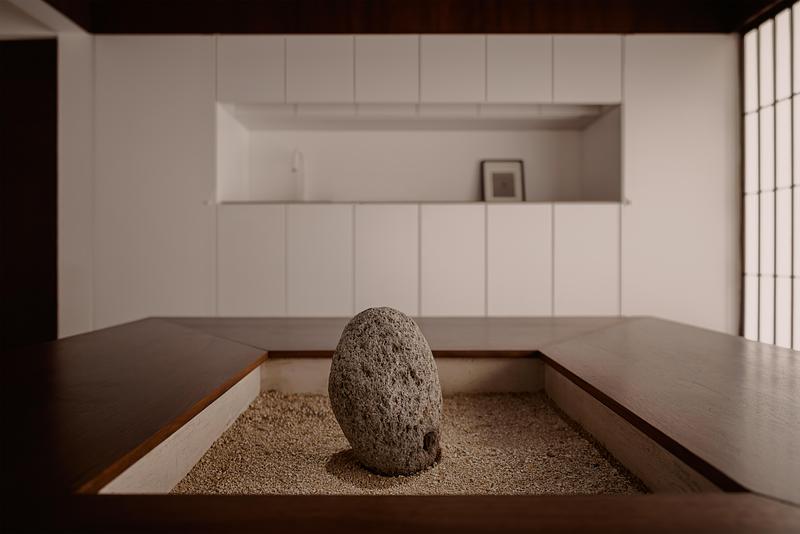 living room gravel pit with single upright dark volcanic stone, surrounding dark walnut wood platforms, matte white flus