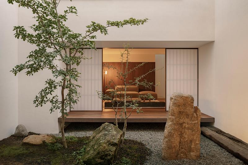 view from stone garden toward living room through open shoji screens, warm amber interior with low dark walnut platform