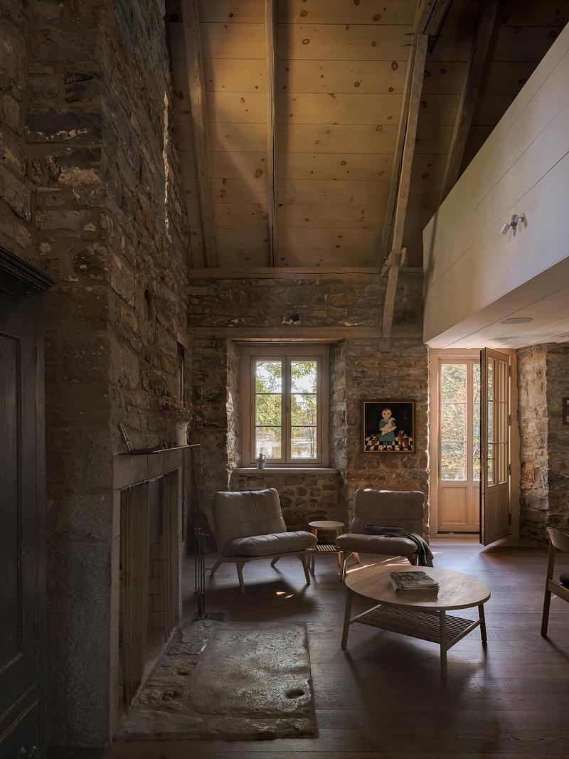 sitting room with rough fieldstone walls, knotty pine beam ceiling, original masonry fireplace, two linen armchairs, she