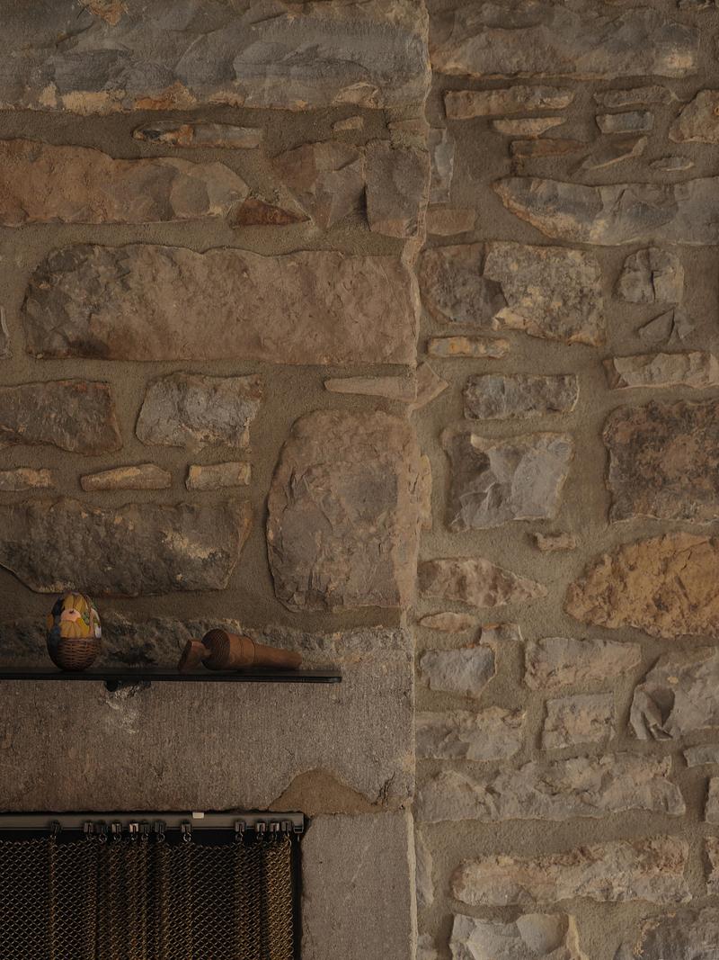 close detail of ancient rubble stone fireplace wall with varied mortar texture, thin dark steel shelf with small ceramic