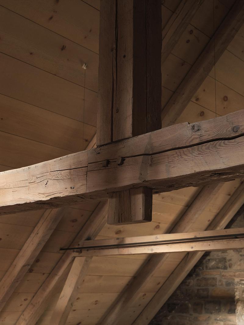 close-up of original dark weathered king-post roof truss joint against pale new pine sarking boards, traditional wooden