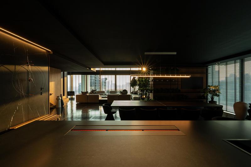 open-plan living and dining zone shot from kitchen end, dark ceiling with linear warm pendant, black stone dining surfac
