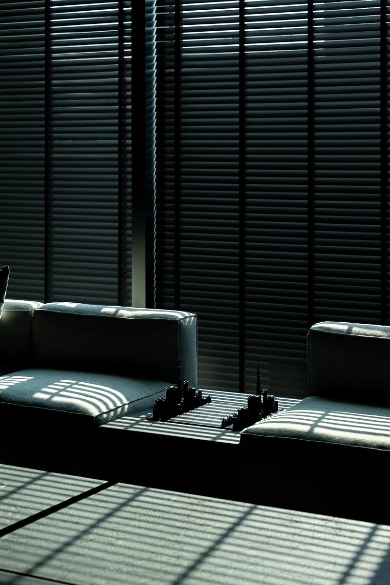 seating nook with two pale grey modular sofa sections flanking dark low table, striped venetian blind shadow falling in