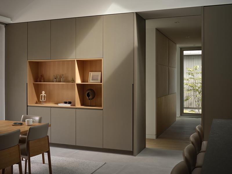dining area matte greige floor-to-ceiling millwork wall with warm oak open shelving recess, small objects on display, co