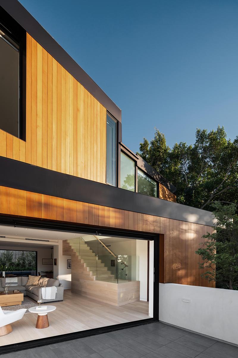 dusk exterior view of two-story cedar-clad house with matte black banding, full-width sliding glass doors open to reveal