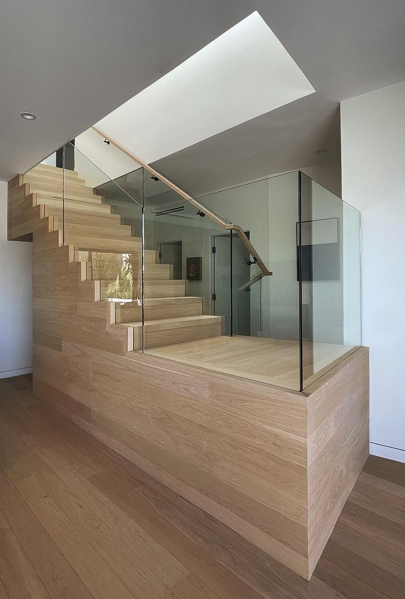 interior stair landing with solid white oak cladding on stringer and landing platform, full-height frameless glass balus