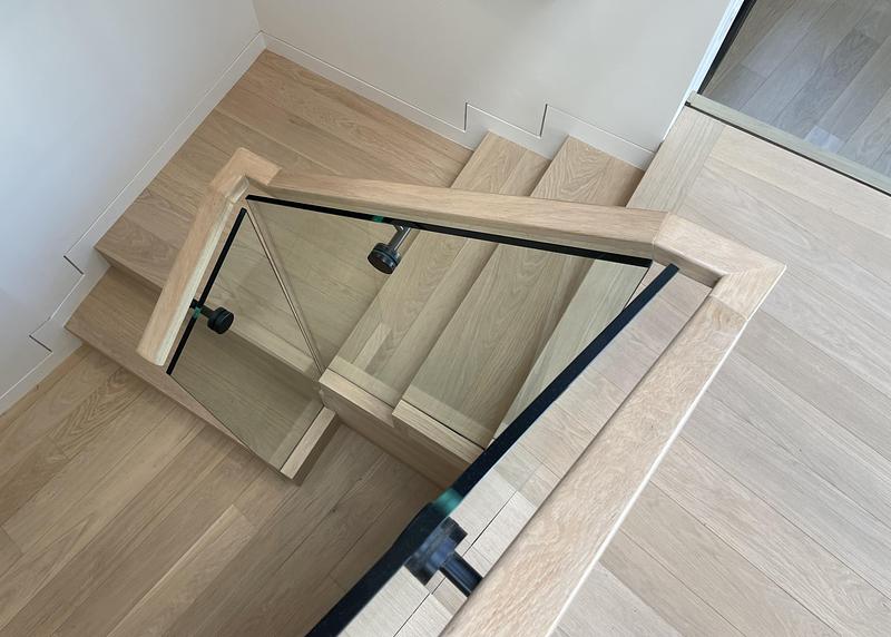 bird's-eye view looking straight down pale oak stair well showing right-angle landing with glass balustrade panels, matt
