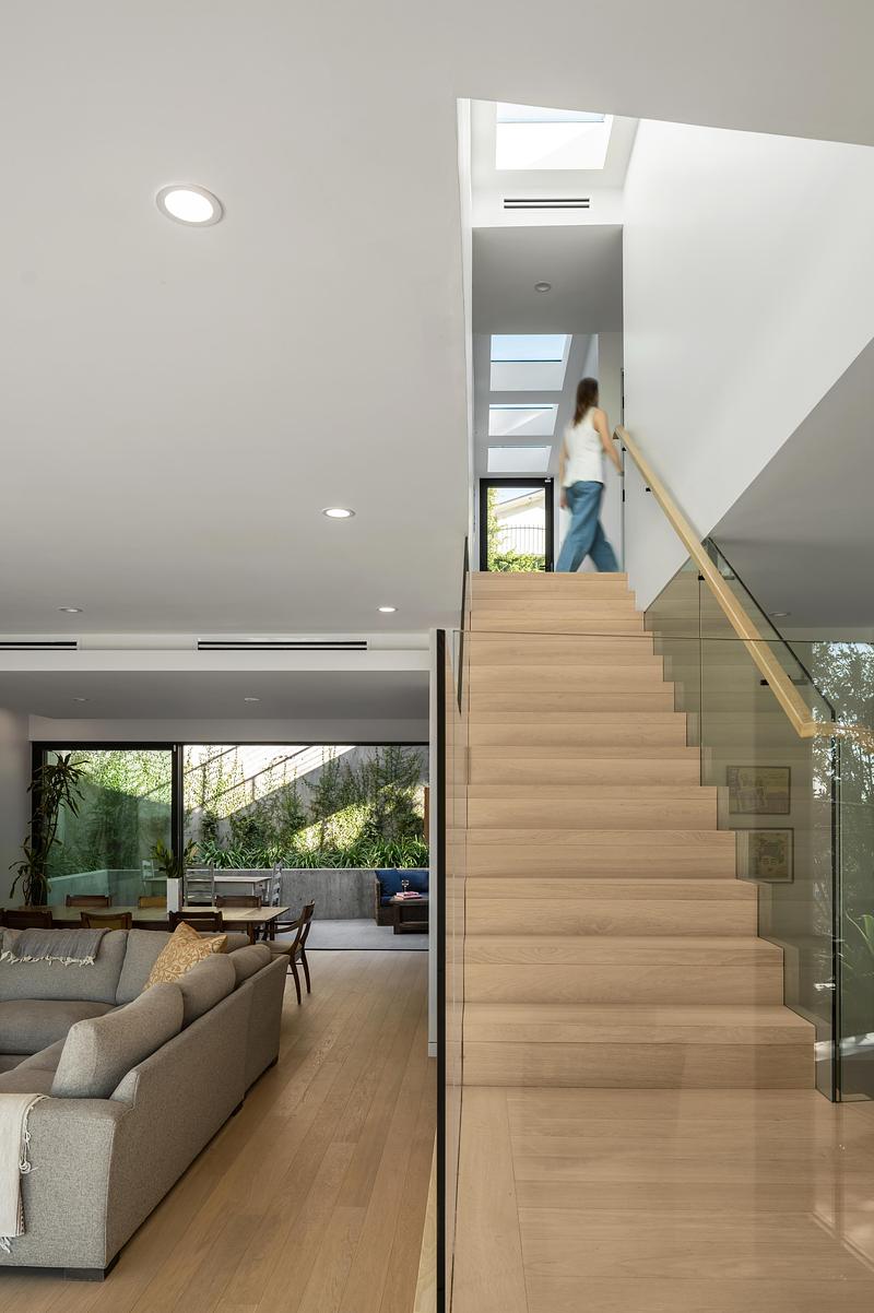 wide interior shot showing pale oak stair with glass balustrade, oak handrail, person ascending with motion blur, living