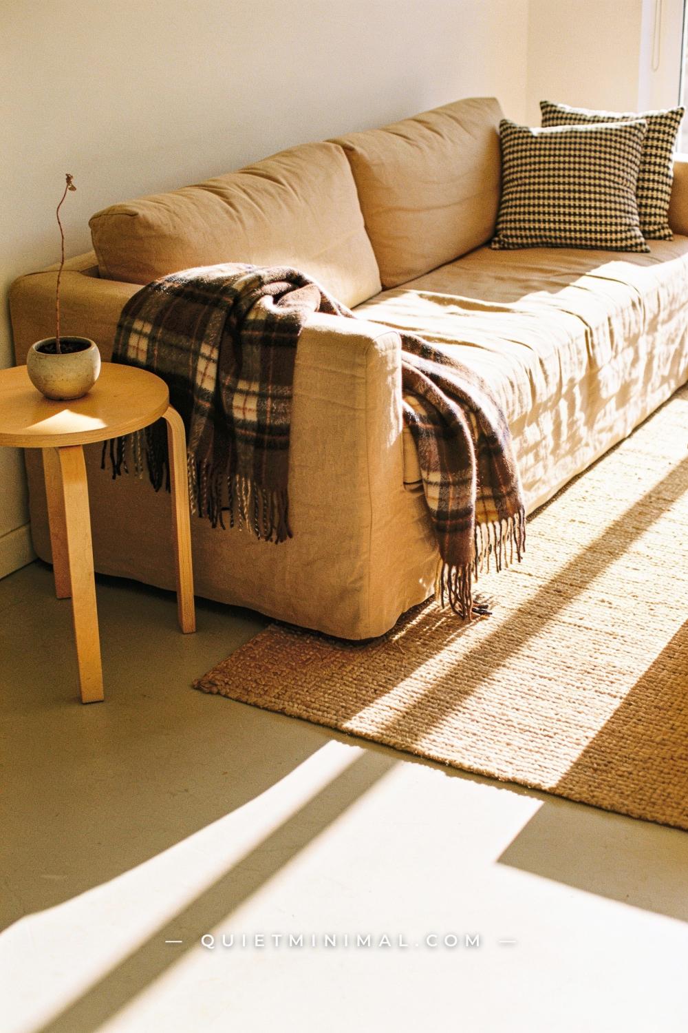 A corner-view establishing shot of a living room seating area — a wide upholstered sofa in warm oatmeal linen dominates