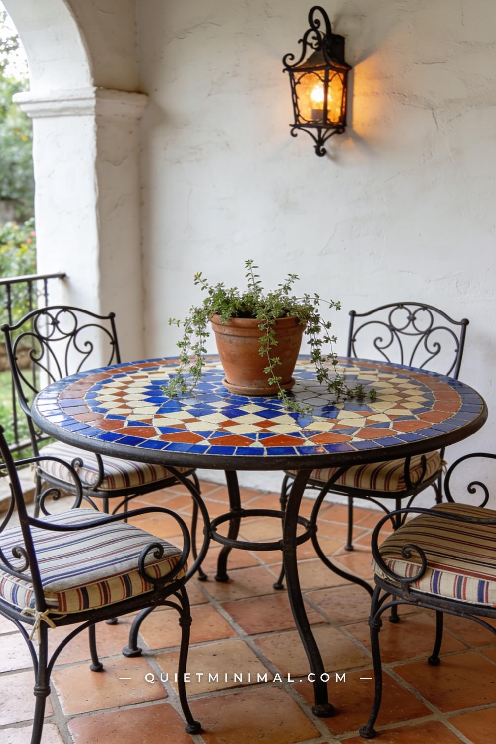 A medium-wide photograph of a Spanish Revival patio dining setup centered on a round table with a hand-painted encaustic