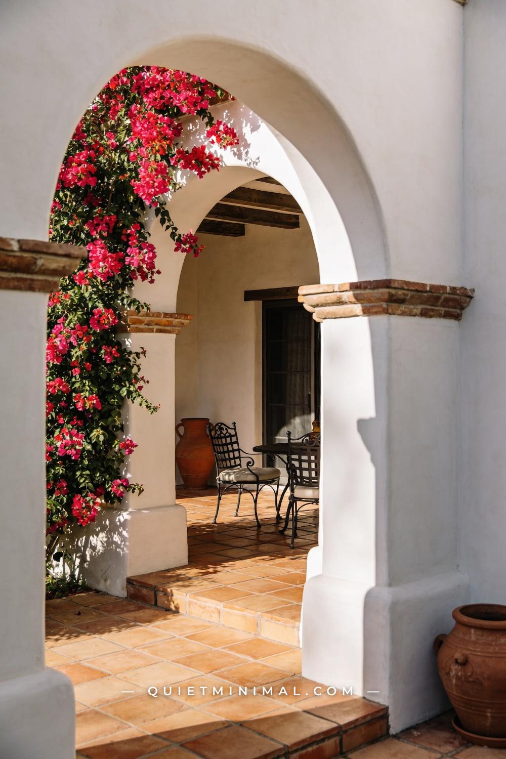 A wide photograph of a Spanish Revival patio entrance framed by a whitewashed stucco arch