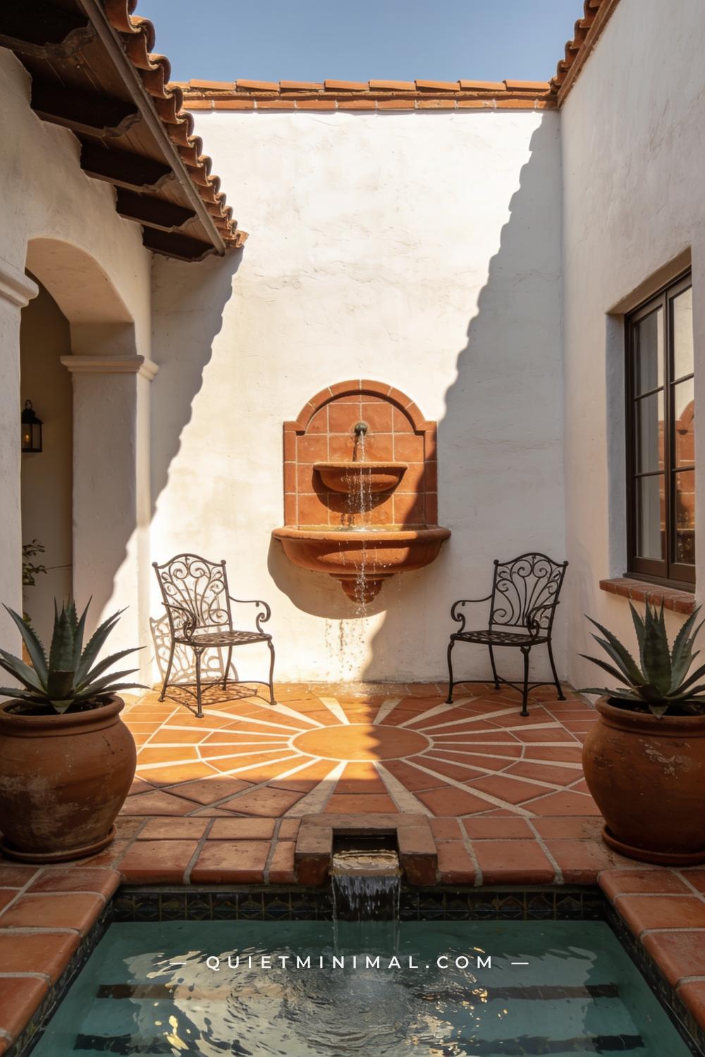 A wide establishing shot of a Spanish Revival patio courtyard centered on a tiered terracotta wall fountain mounted on a