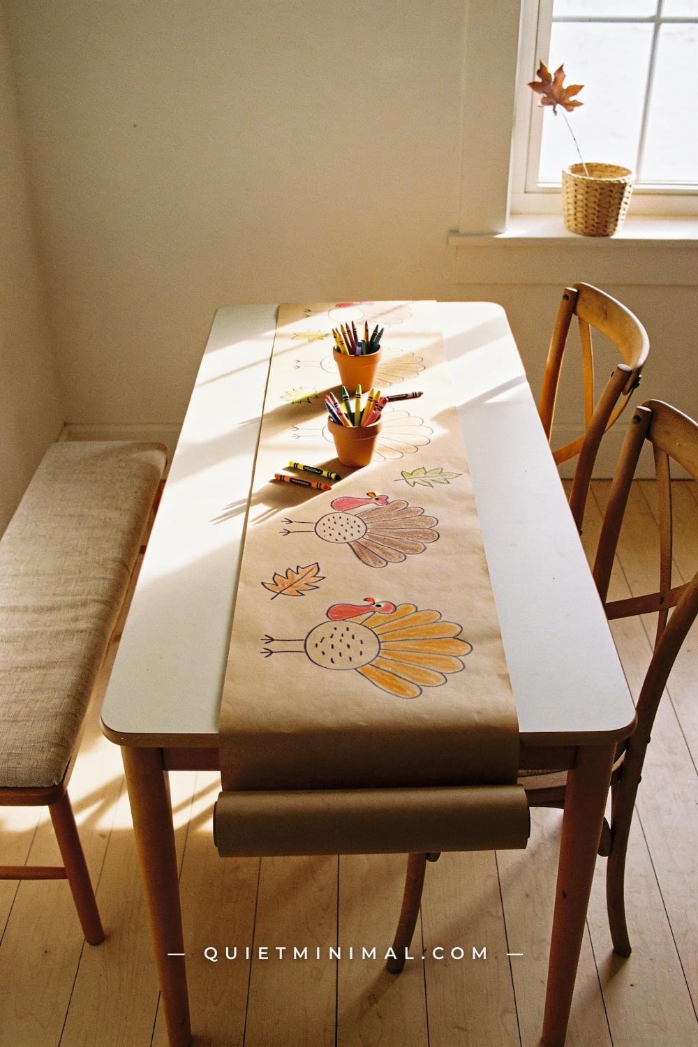 A wide establishing shot taken from across the room showing a rectangular kids dining table covered end-to-end with a lo
