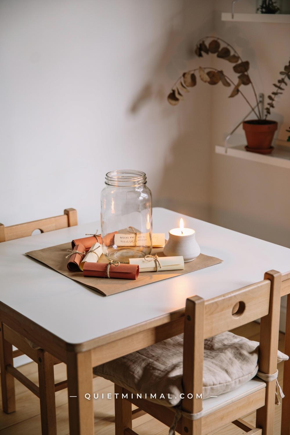 A wide establishing shot from a straight-on wall view of a kids dining table showing a central clear glass jar surrounde